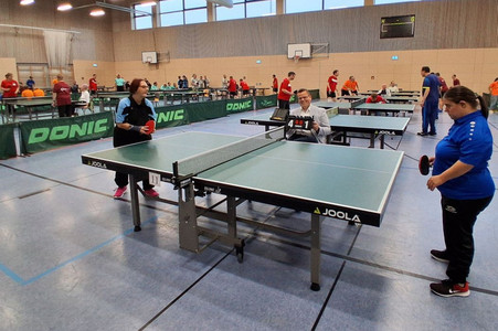 Zu sehen ist die Halle mit Spielerinnen und Spielern an Tischtennisplatten.